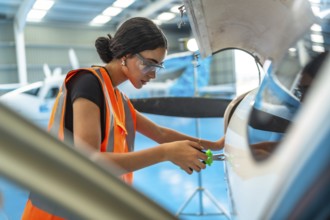 Technician in a hangar performing maintenance on an aircraft engine, wearing safety gear and using