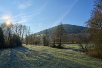 The sky illuminates a meadow and trees in front of a wooded hill, Kirchzell, Amorbach, Odenwald,