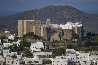 Stone castle towers over a village with white houses and surrounding mountains, Monastery of St