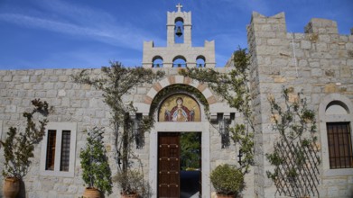 Stone building with bell tower and religious mosaic, surrounded by climbing plants, woman's