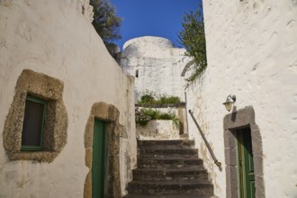 Whitewashed buildings with stone details and green doors under a clear blue sky, Monastery of the