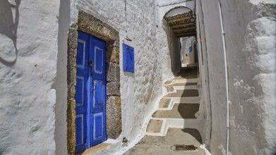 Narrow, sunny alley with blue doors in traditional white Mediterranean architecture, Mantomata