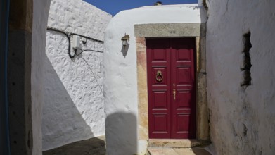 A winding entrance with a striking red door and stone walls, illuminated by a small lantern,
