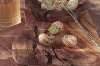 Snails cooked with herb oil on a wooden plate, served with white wine, natural light, no people