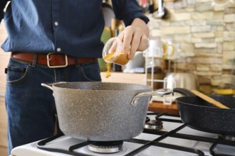 A person pouring spices into a pot on a stove. The countertop is lined with cooking utensils, and a