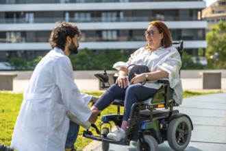 Doctor adjusting the footrest of an electric wheelchair for a smiling woman, enjoying a sunny day