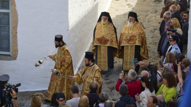 Priests in costly vestments lead a procession through a crowd as people watch and take photos,
