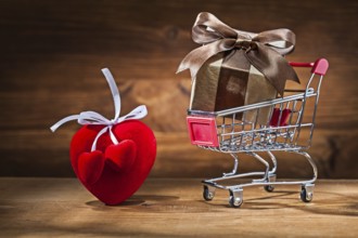 Gift box in shopping trolley and Valentine's heart toy on vintage wood