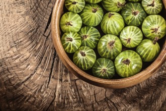 Ripe gooseberries in round bowl on vintage wooden background