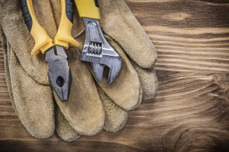 Leather safety gloves adjustable spanner pliers on wooden board construction concept