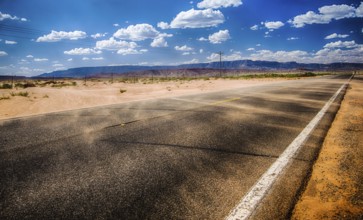 black asphalt highway with wind gust blowing red sand across inthe northern Arizona desert in the