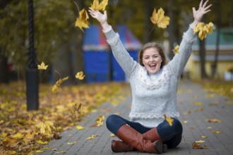 Beautiful girl in the autumn park scatters yellow leaves