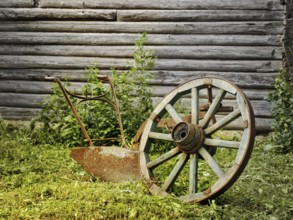 Wheel and plough on the grass near the wooden wall