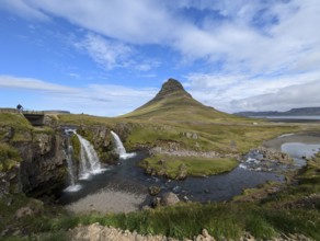Landscape with a mountain and a waterfall flowing into a river under a blue sky with clouds.