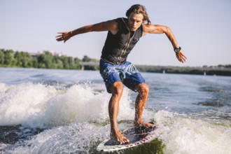 Active wakesurfer jumping on wake board down the river waves. Surfer on wave. Male athlete training