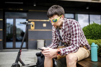 Individual urban environmental friendly transport electric kick scooter parked near man sitting on