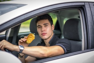 Young handsome man driving his car while eating food in the traffic