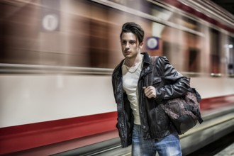 Handsome young male traveler in train station with backpack, looking to a side