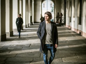 Elegant attractive young man outdoor wearing wool coat, in European city under colonnade in city