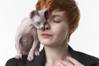 Redhead woman with closed eyes and playful kitten standing on shoulder, gently pressed against face