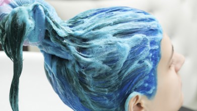 Professional hairdresser holds client's long blue hair in hand while washing hair after process of