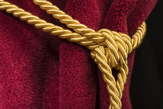 Red velvet curtain with tassel. Close up knot on rope
