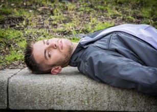 Portrait of handsome young man looking to a side while lying on bench in city park