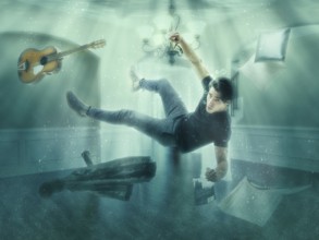 Illusion of man floating underwater among objects in room looking at camera