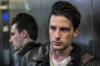 Handsome young man leaning against mirror inside an elevator or lift, looking at camera