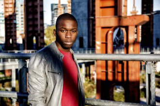 Portrait of a sexy young black man in urban environment wearing red shirt and grey leather jacket