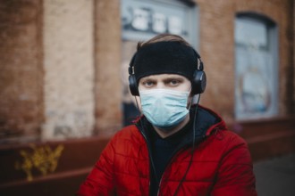 Man wearing a mask and headphones stands against a brick wall