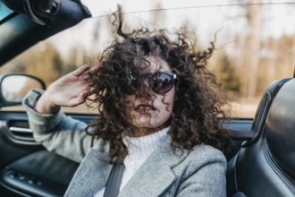 Woman with curly hair and sunglasses sitting in a car on a sunny day