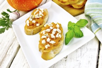 Bruschetta with pumpkin, salted feta cheese in a plate, garlic, basil and parsley, towel and orange