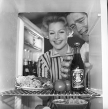 In the kitchen 1950s. A couple in their kitchen and at the refrigerator where the food and beer is