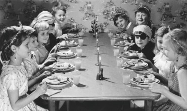 Children in the 1950s. Girls and boys dressed up in hats and costumes are sitting a table together