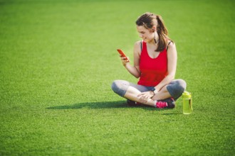 Theme sport health. beautiful young girl sitting resting on green grass lawn stadium using