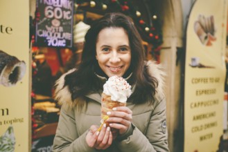 A beautiful girl in a warm jacket eats trdelnik or Trdlo with cream in her hands, in the winter in