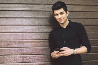 Portrait of young handsome Turkish male model. Mediterranean race brunette in black shirt is using