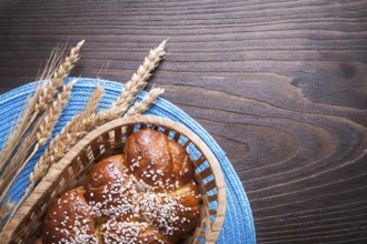 Sweet roll in wicker basket wheat rye ears with wattled table-cloth on wooden vintage board food