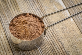 Cacao powder in a metal measuring scoop against grunge wood background