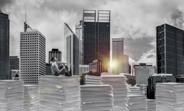 Thoughtful businessman sitting on pile of documents and looking away with cityscape and sunlight on