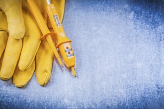 Yellow electrical tester safety gloves on metallic background electricity concept