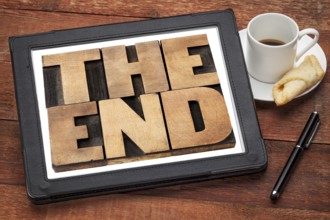 The end - text in vintage letterpress wood type on a digital tablet with a cup of coffee