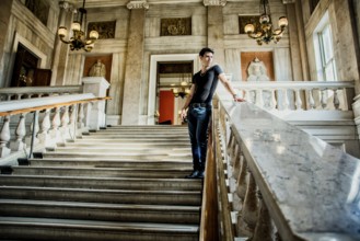 Young Handsome Man Standing on Stairs and Leaning Against Rail Inside an Architectural Building