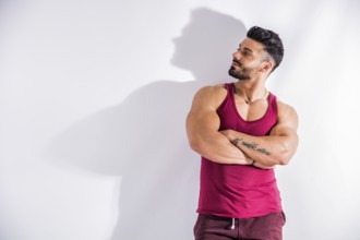 Muscular bodybuilder leaning against white wall, looking at it as if reading something, with large
