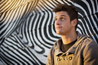Attractive young man standing against zebra pattern graffiti wall, looking up