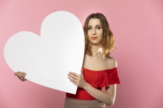 A beautiful girl in love holds a heart shape in her hand. Young woman wants to give a beautiful