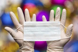 Doctor hands holding medical face mask in white gloves on background bokeh Happy New Years balls