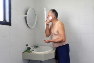 Man 60 plus shaves wet in the bathroom