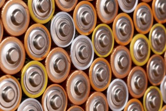 Multiple used AA alkaline batteries are seen arranged in a pile. Closeup side view from the plus